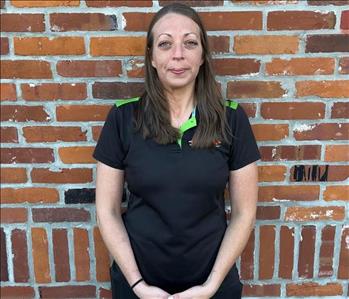 woman in black SERVPRO shirt standing in front of brick wall