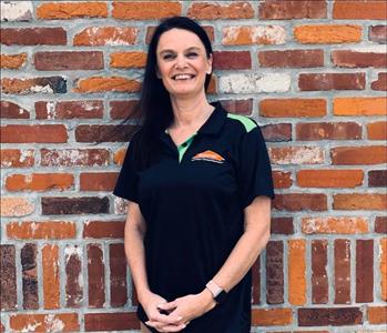 woman in black SERVPRO branded t-shirt and khaki pants standing in front of brick wall