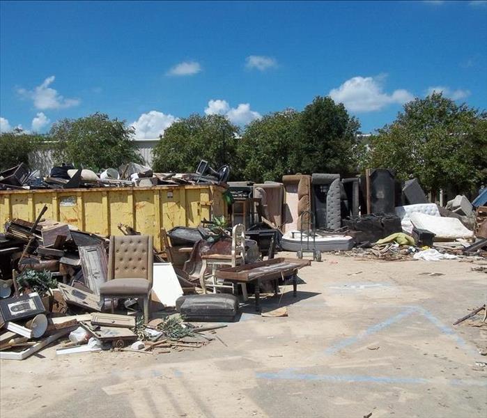 piles of broken furniture outside of full yellow dumpster