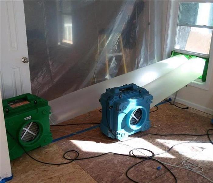 green fan and blue fan with plastic cylinder hoses pumping air our of window 