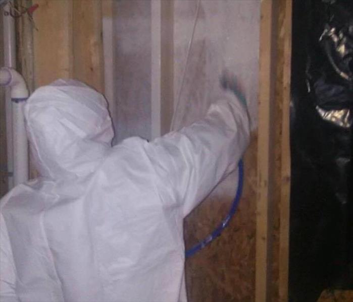 person in white hazmat suit spray white sealer on wall without sheetrock 