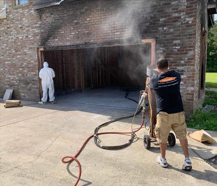 open garage with fire damage on outside brick with two technicians cleaning