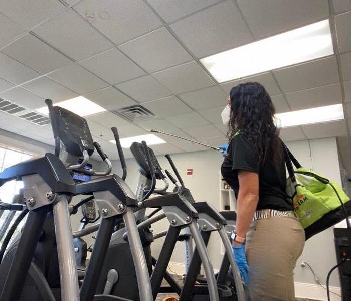 woman spraying around ellipticals in gym 