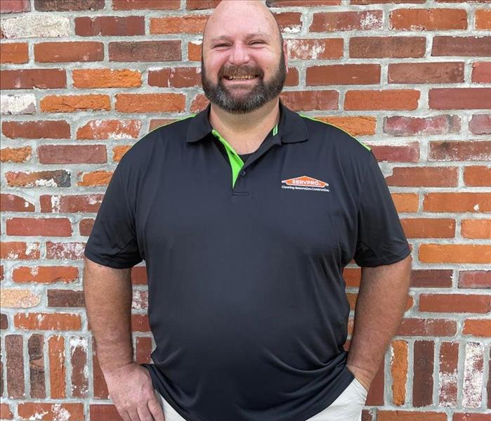 man with servpro shirt and khakis pants standing in front of brick wall